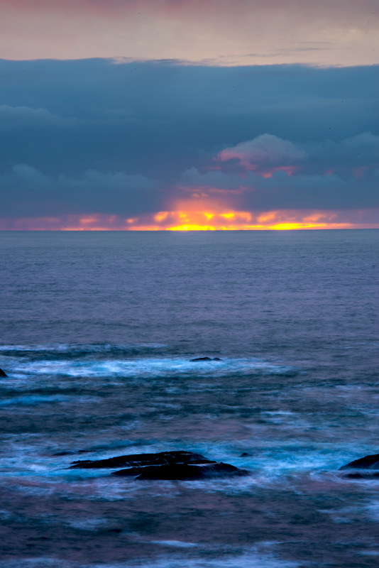 Minimalist long exposure coastal shot with a razor-thin line of fire on the horizon over the Pacific Ocean
