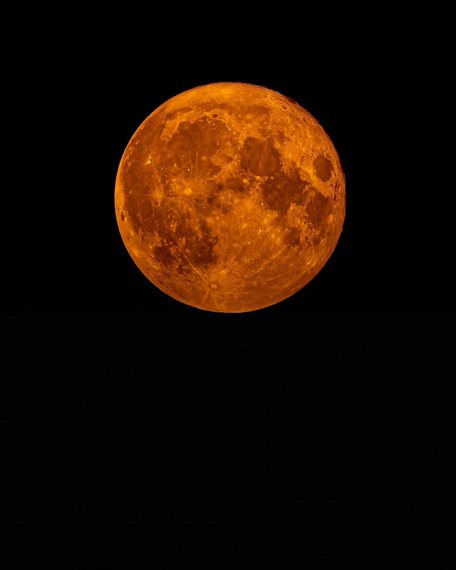 Large blood moon glowing deep amber against a pure black sky