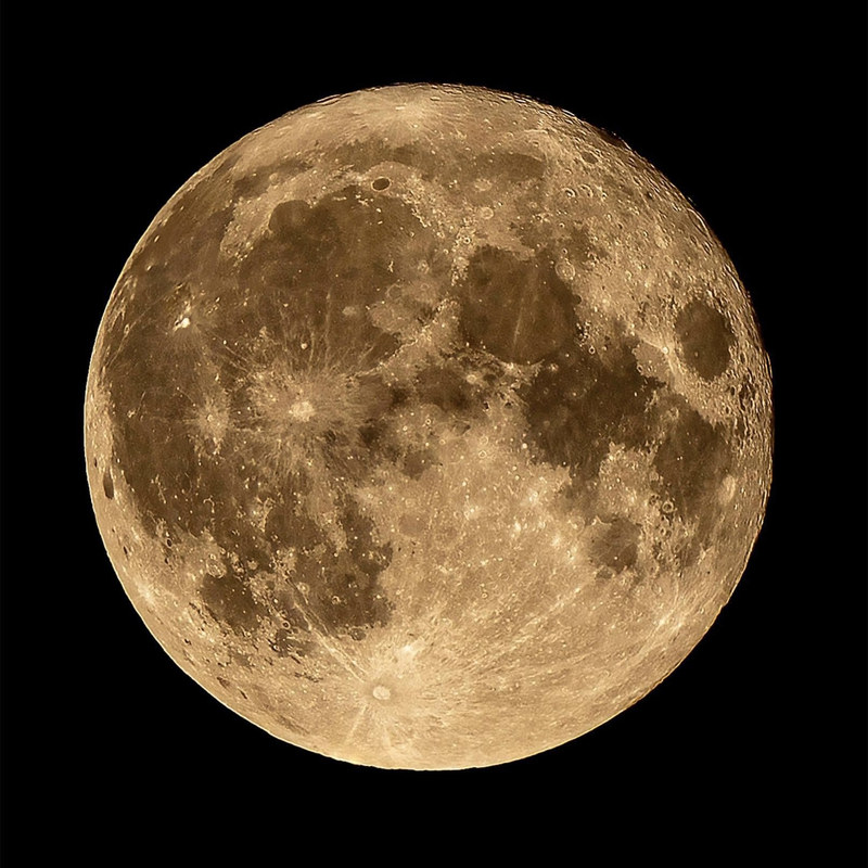 Full moon in golden tones with sharp crater detail against black sky